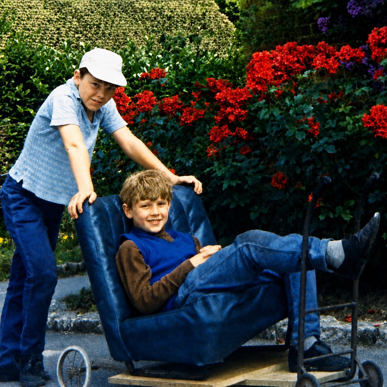 Richard driving Mike's homemade go-kart beside rose bushes in 1971