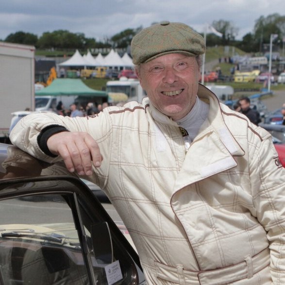 Mike smiling beside a racing car in his racing overalls in 2019